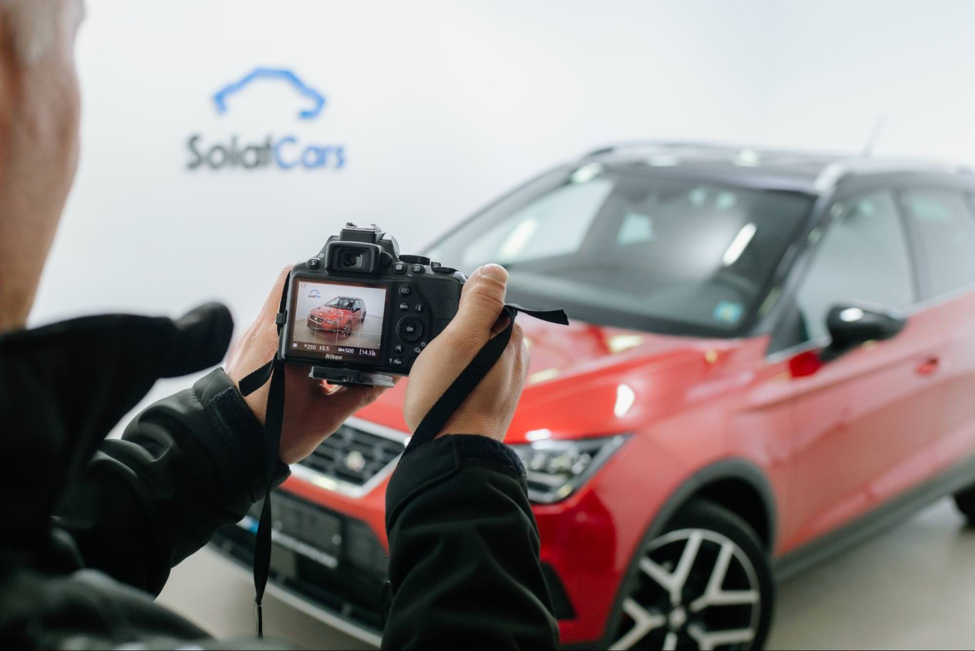 Eine Person hält eine Kamera und macht in einem Autostudio ein Foto von einem Auto