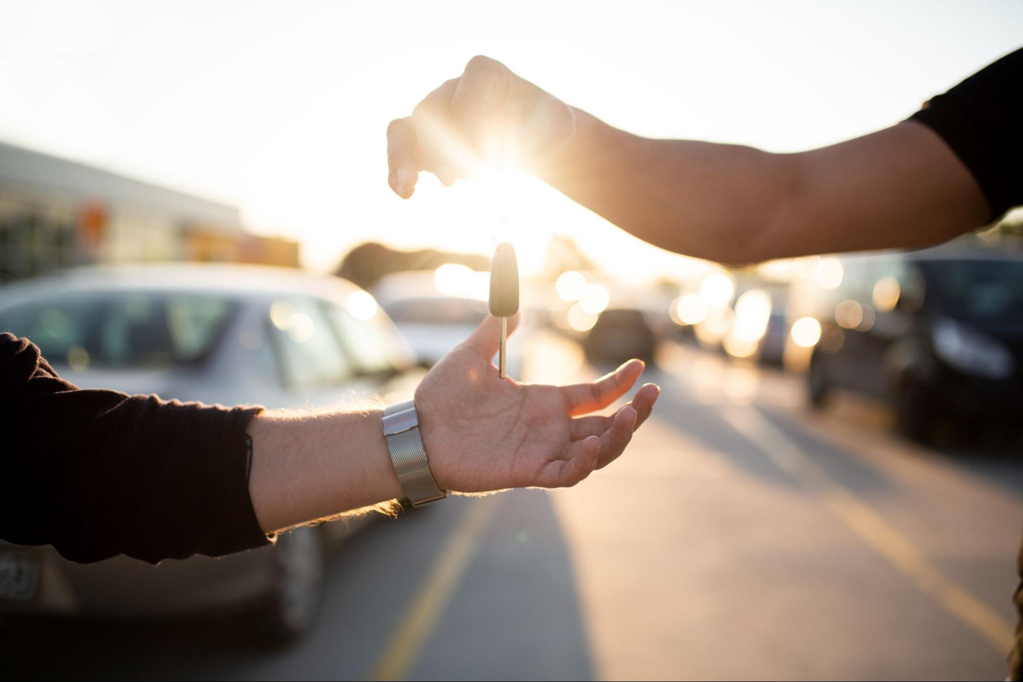 une main déposant les clés de voiture dans une autre main avec le coucher du soleil en arrière-plan