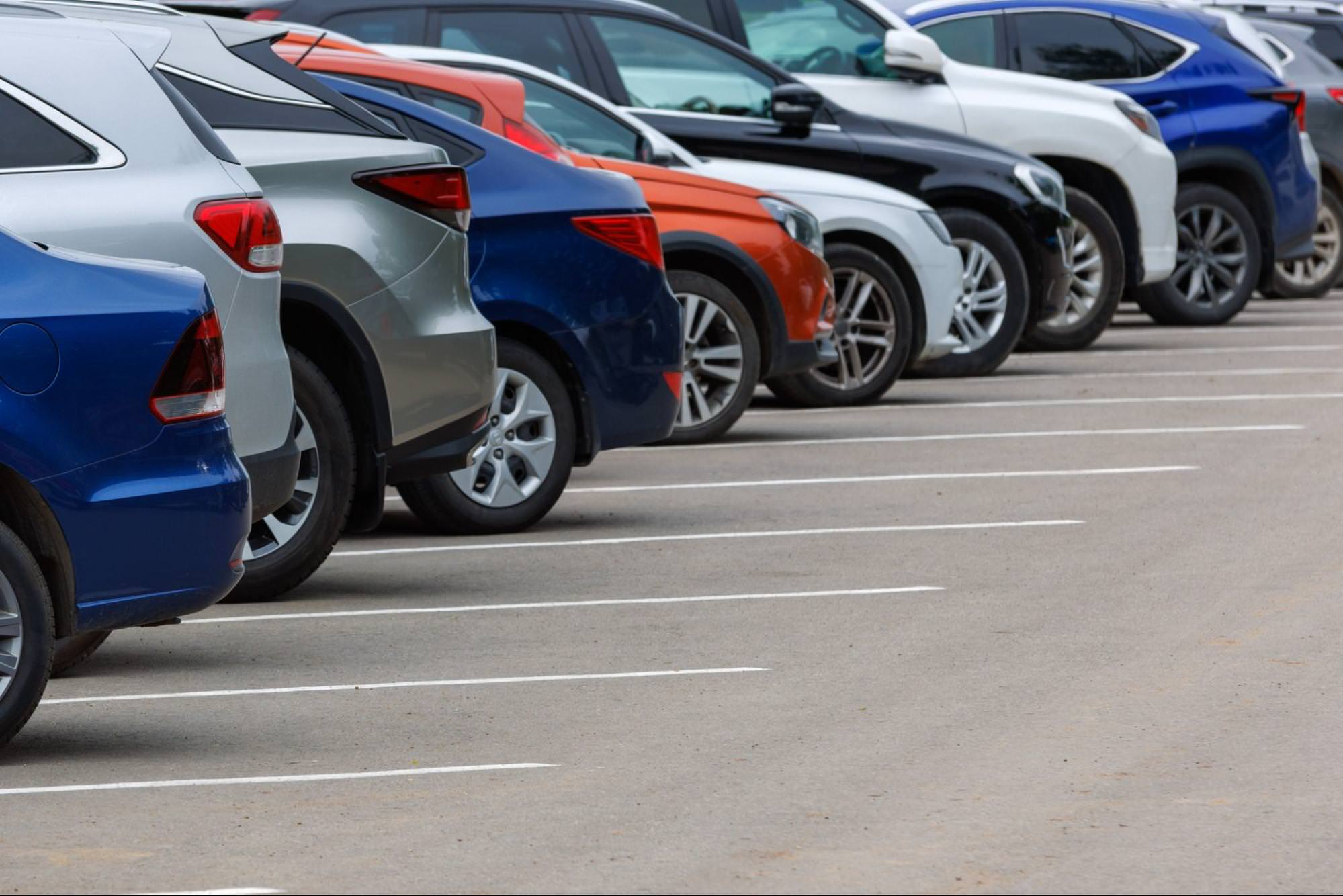 Reihe verschiedenfarbiger Autos auf einem asphaltierten Parkplatz