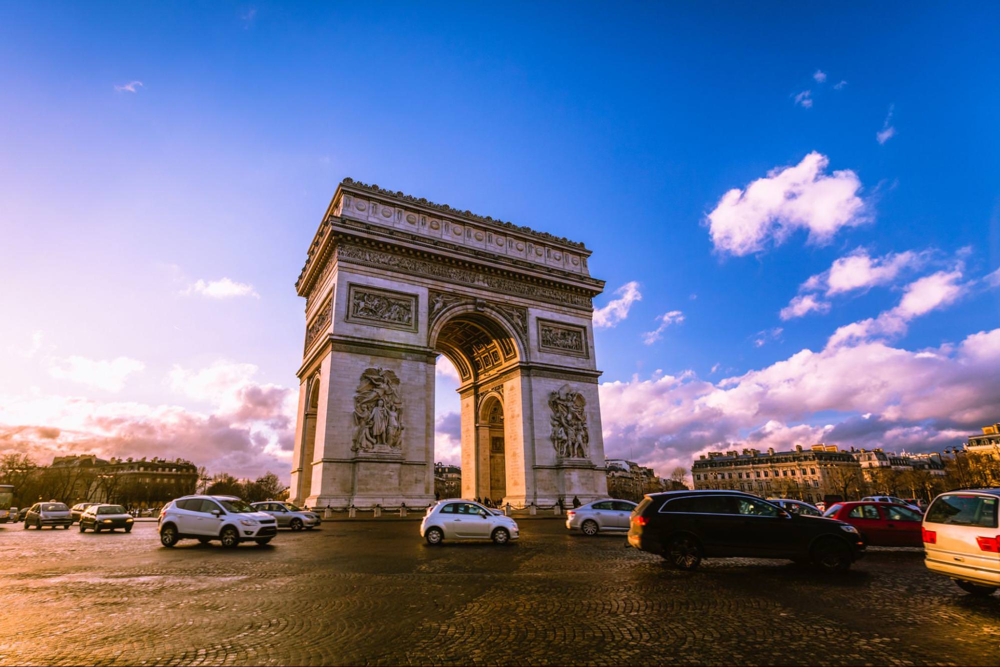 Slavný Arc de Triomphe v Paříži, Francie při západu slunce s automobilovým provozem kolem něj.