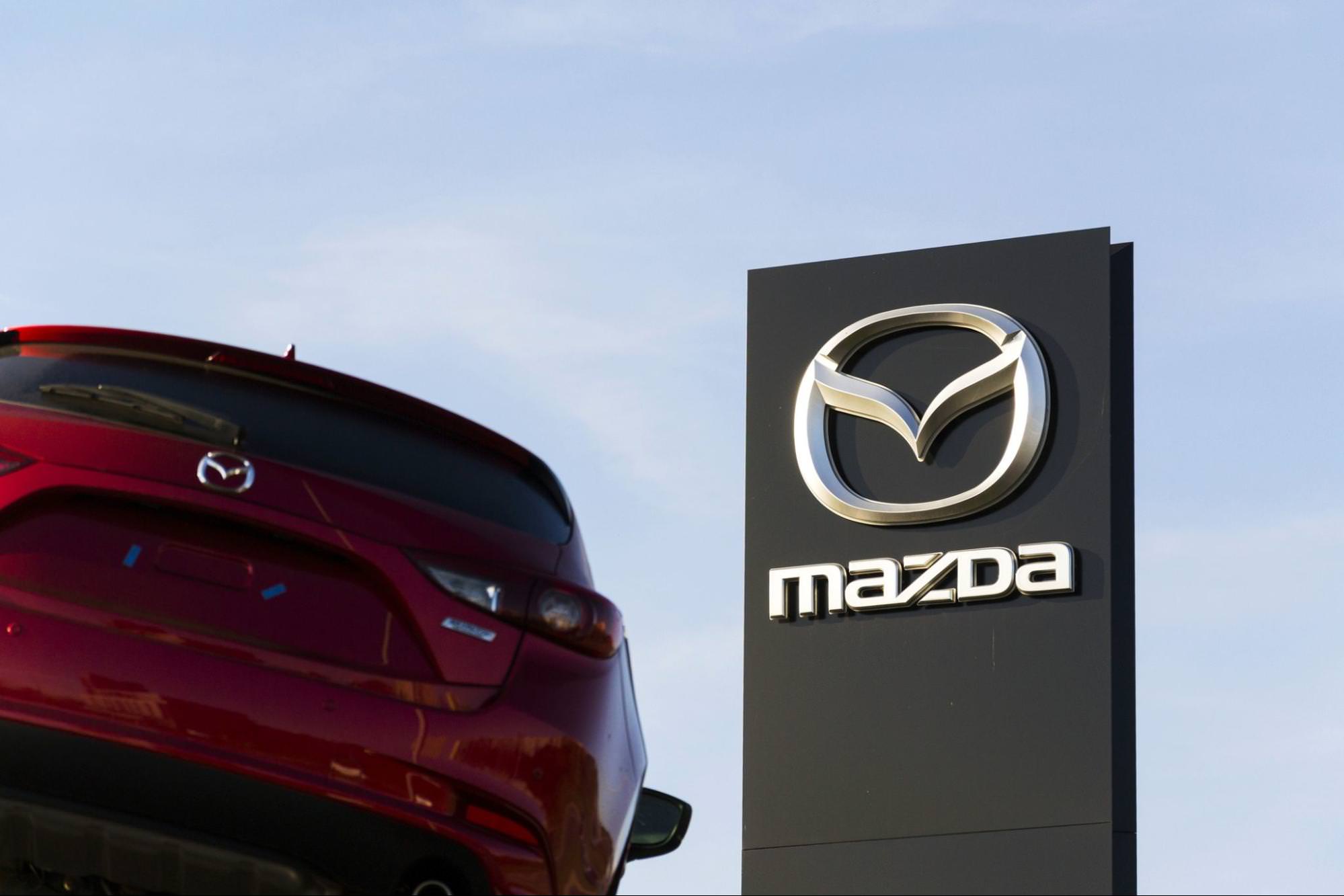 вид логотипа Mazda на автомобиле и на заднем плане