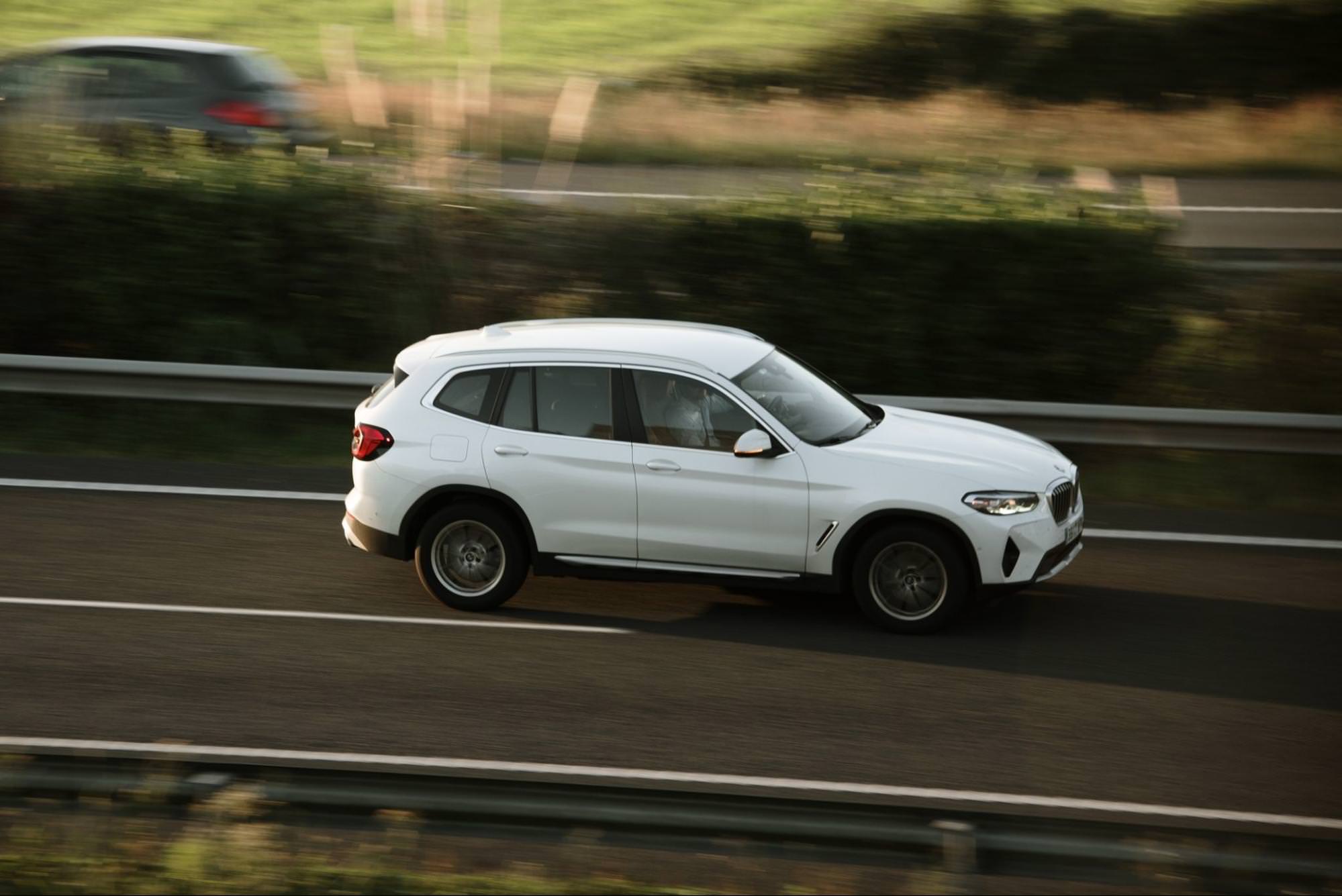 Biały SUV BMW X3 jadący autostradą, uchwycony w ruchu z rozmytym tłem.
