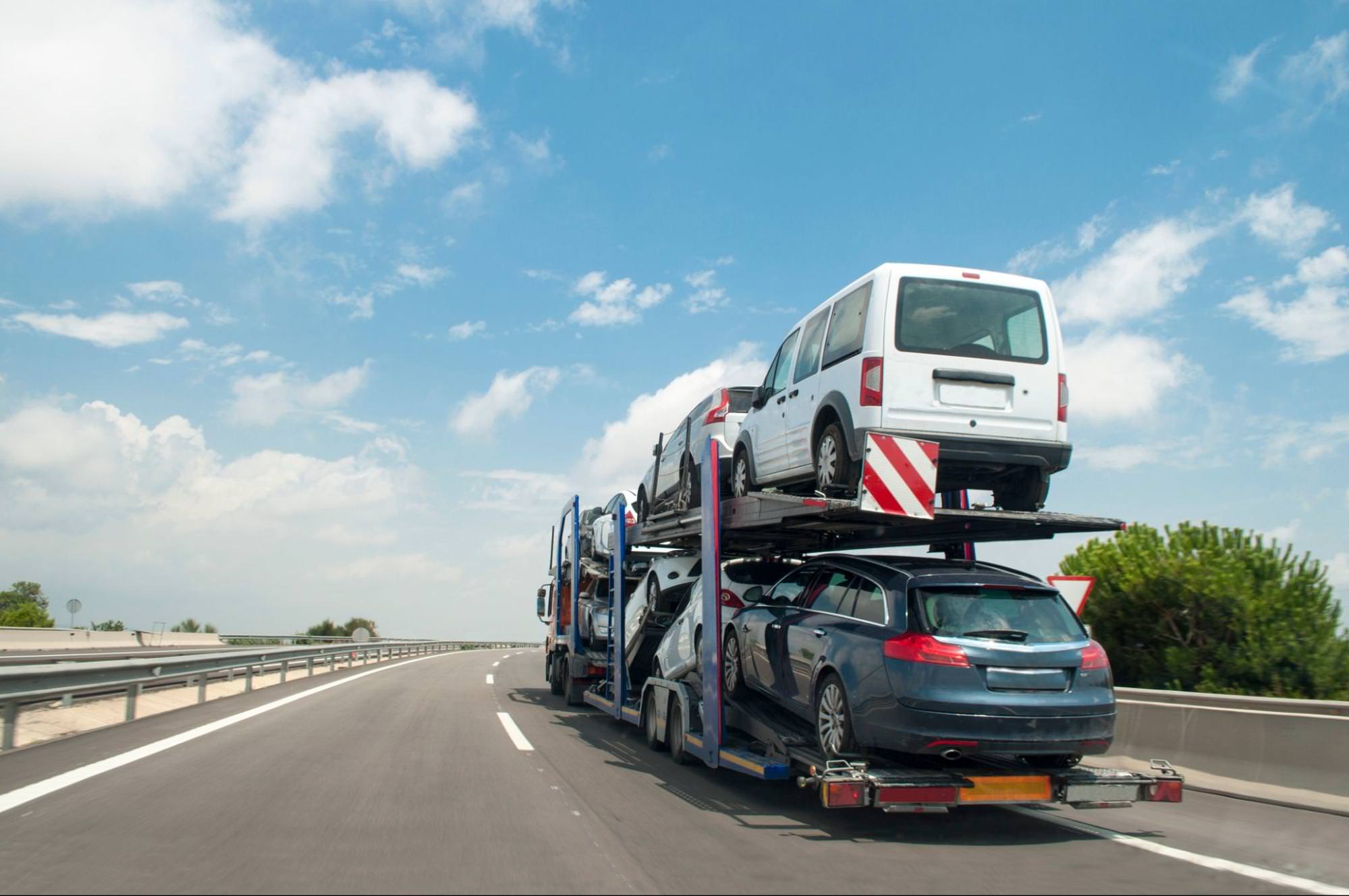 Car transporter carrying multiple vehicles on a highway, representing the shipment of cars from Belgium to Portugal