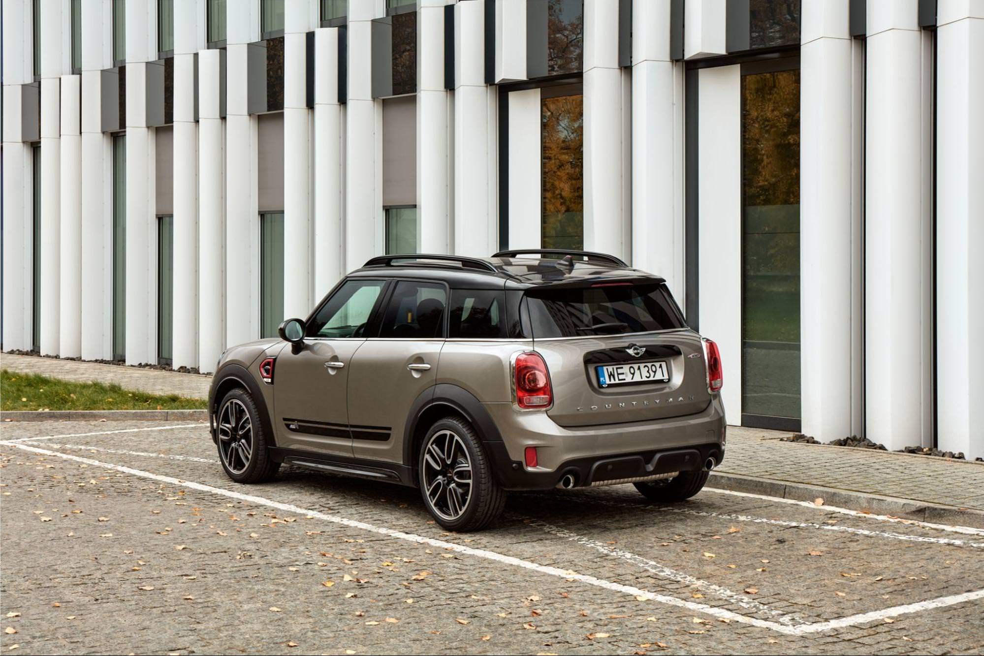 Une Mini Countryman beige, le plus grand modèle SUV de la marque, garée devant un immeuble moderne aux colonnes blanches. L'image met en évidence la taille accrue du Countryman et son style plus robuste par rapport aux modèles Mini traditionnels.