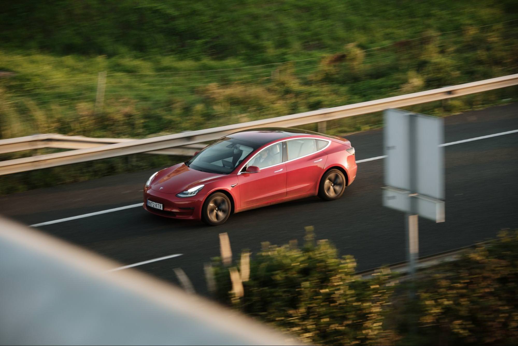 A red Tesla Model 3 electric vehicle driving on a highway