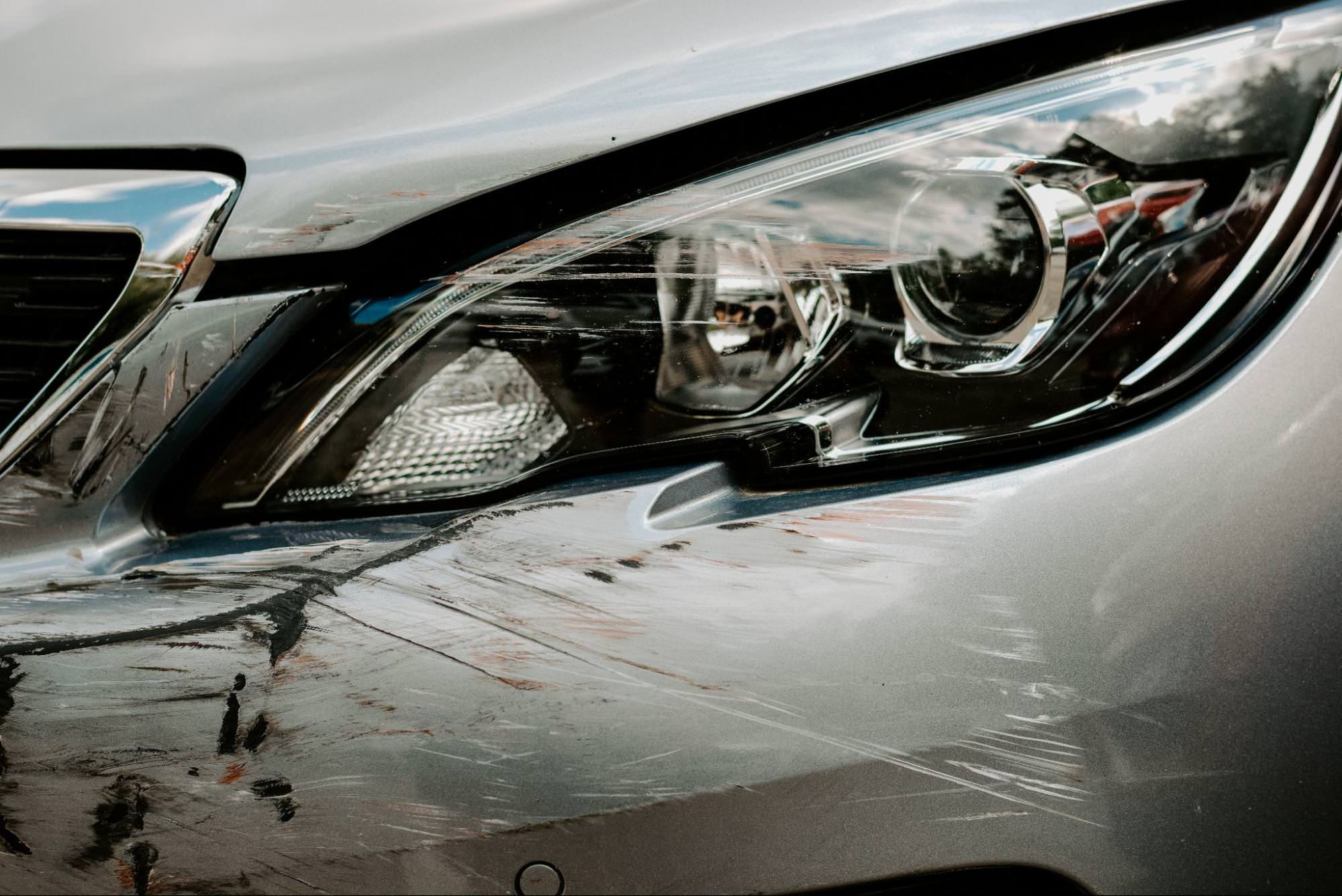 close up of a grey car with scratch damage around one of the lights and front bumper