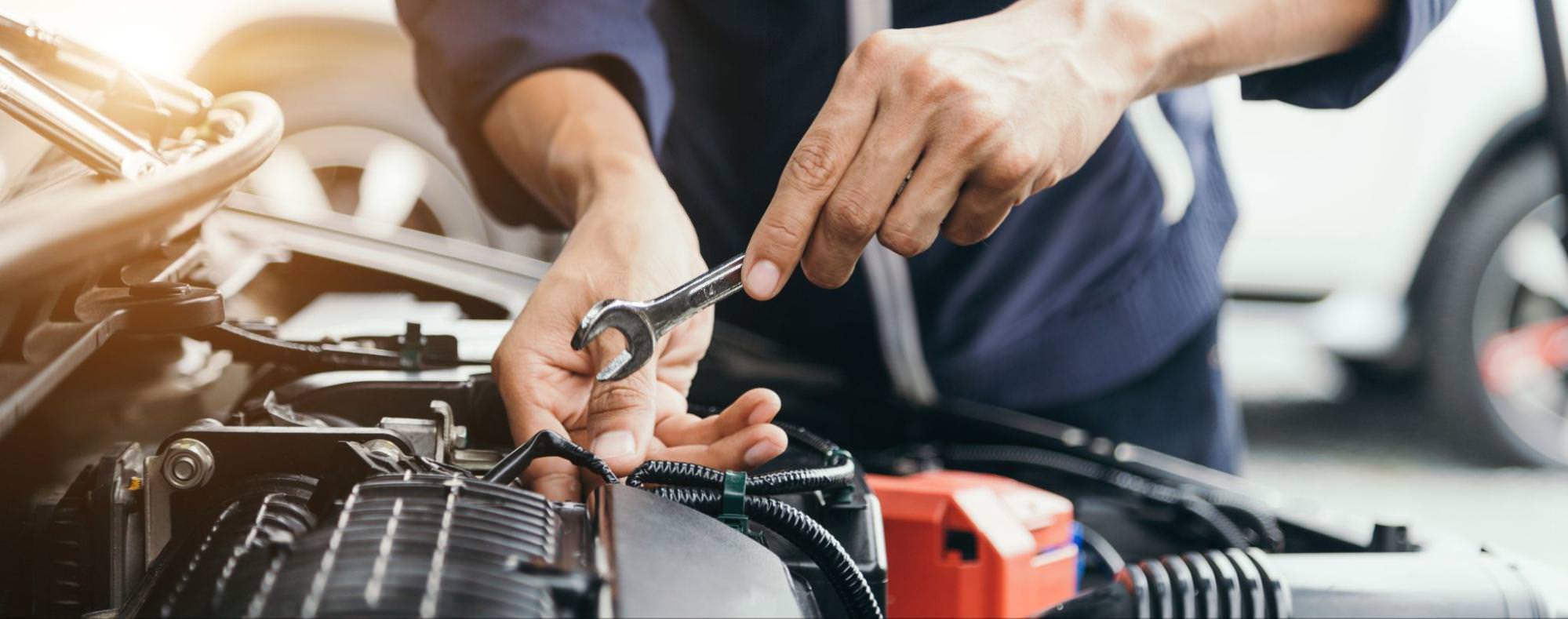 close up of mechanic's hands working on the engine of car with a wrench