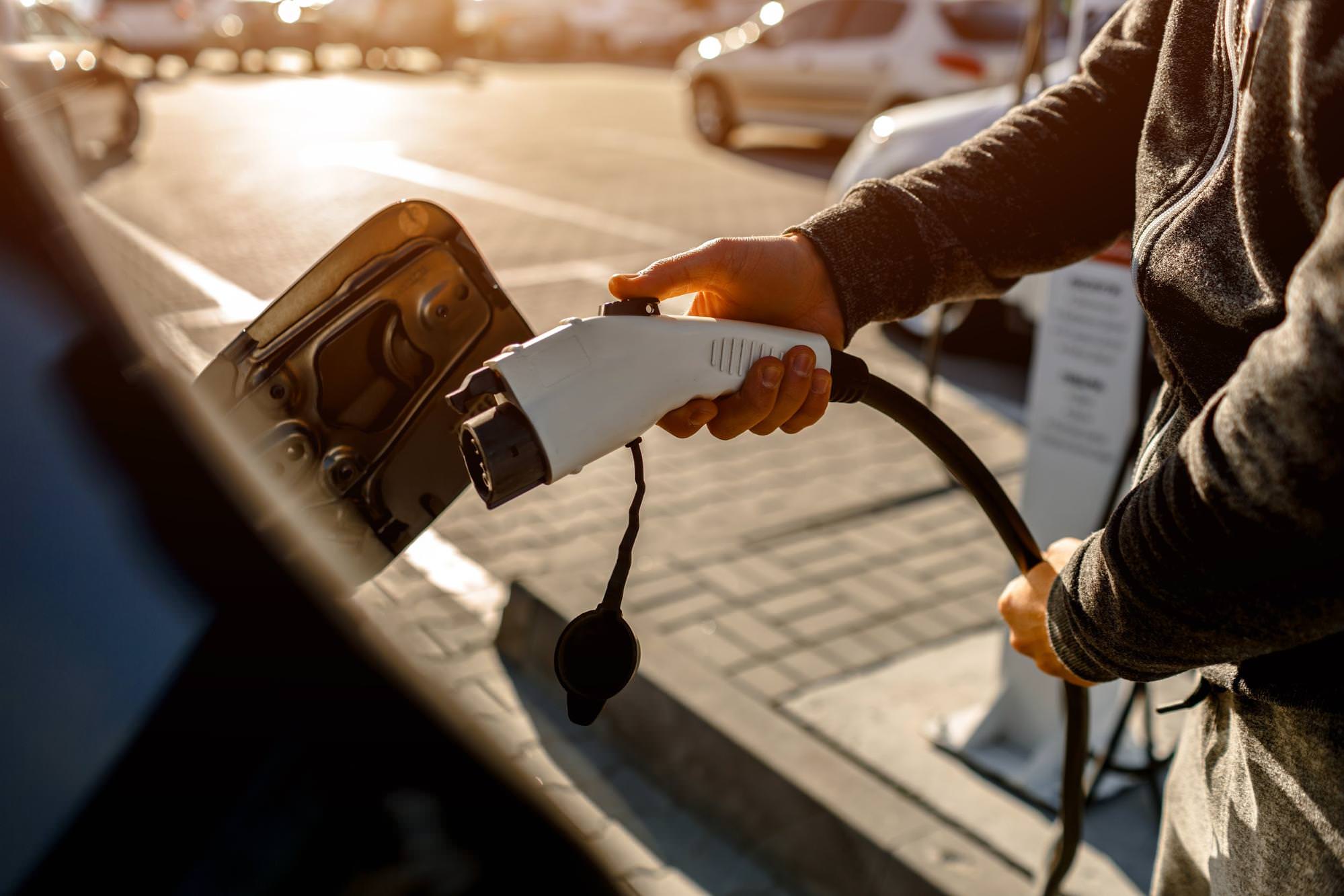 Muž držící nabíjecí kabel pro elektromobil na venkovním parkovišti