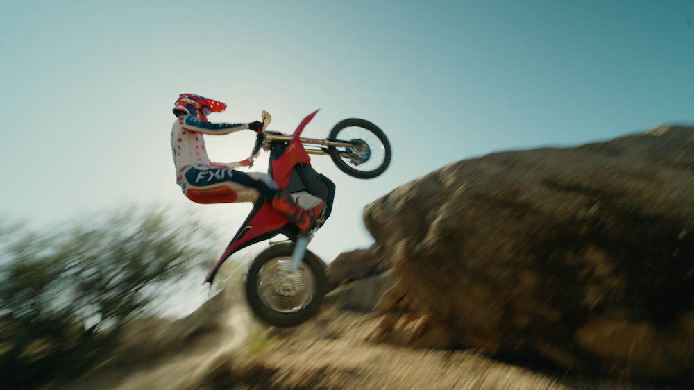 Cooper Abbott pulling a wheelie on the Stark VARG EX, dust kicking up against Arizona boulders.
